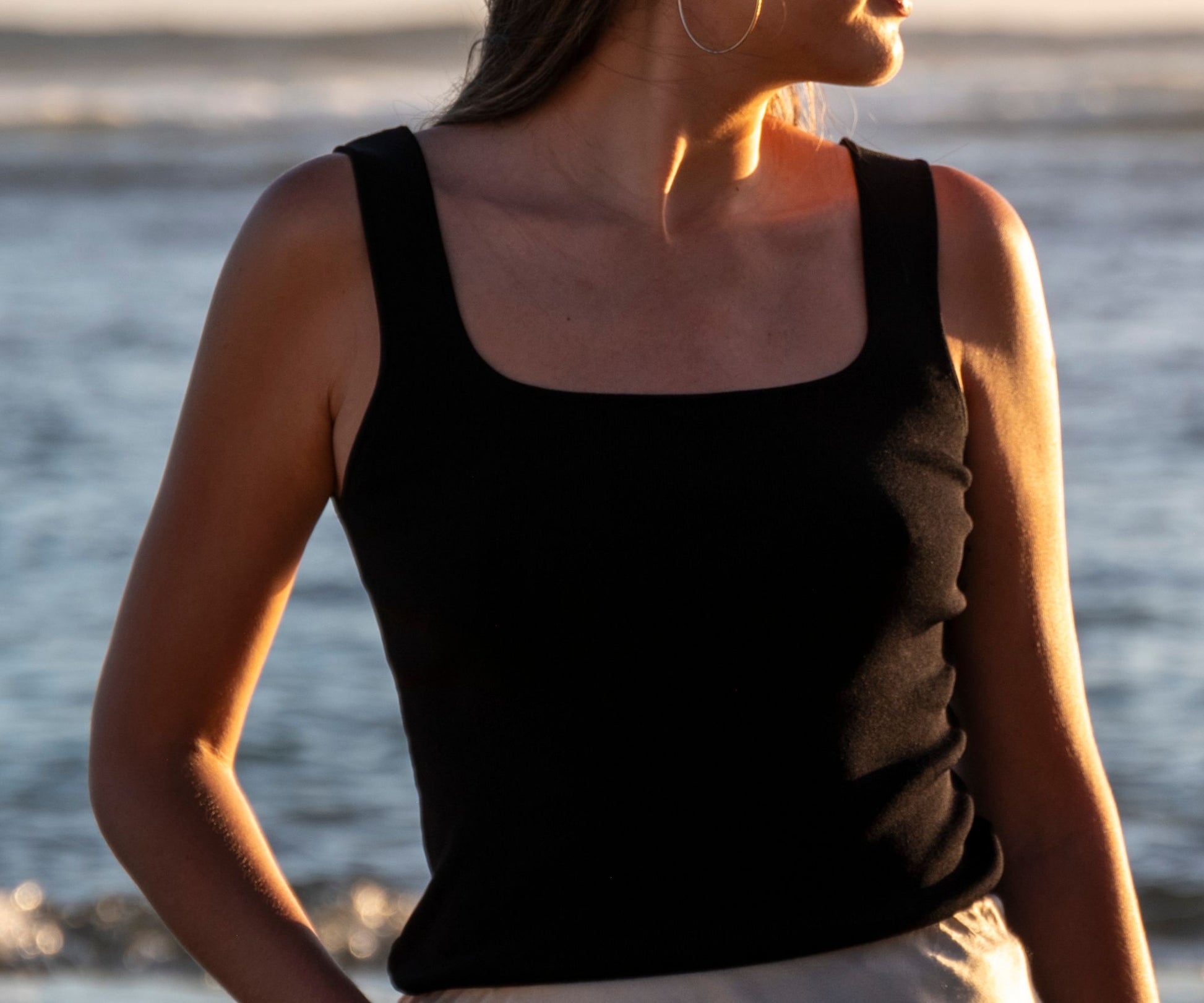 Femme portant un débardeur col carré noir avec la mer en arrière plan 