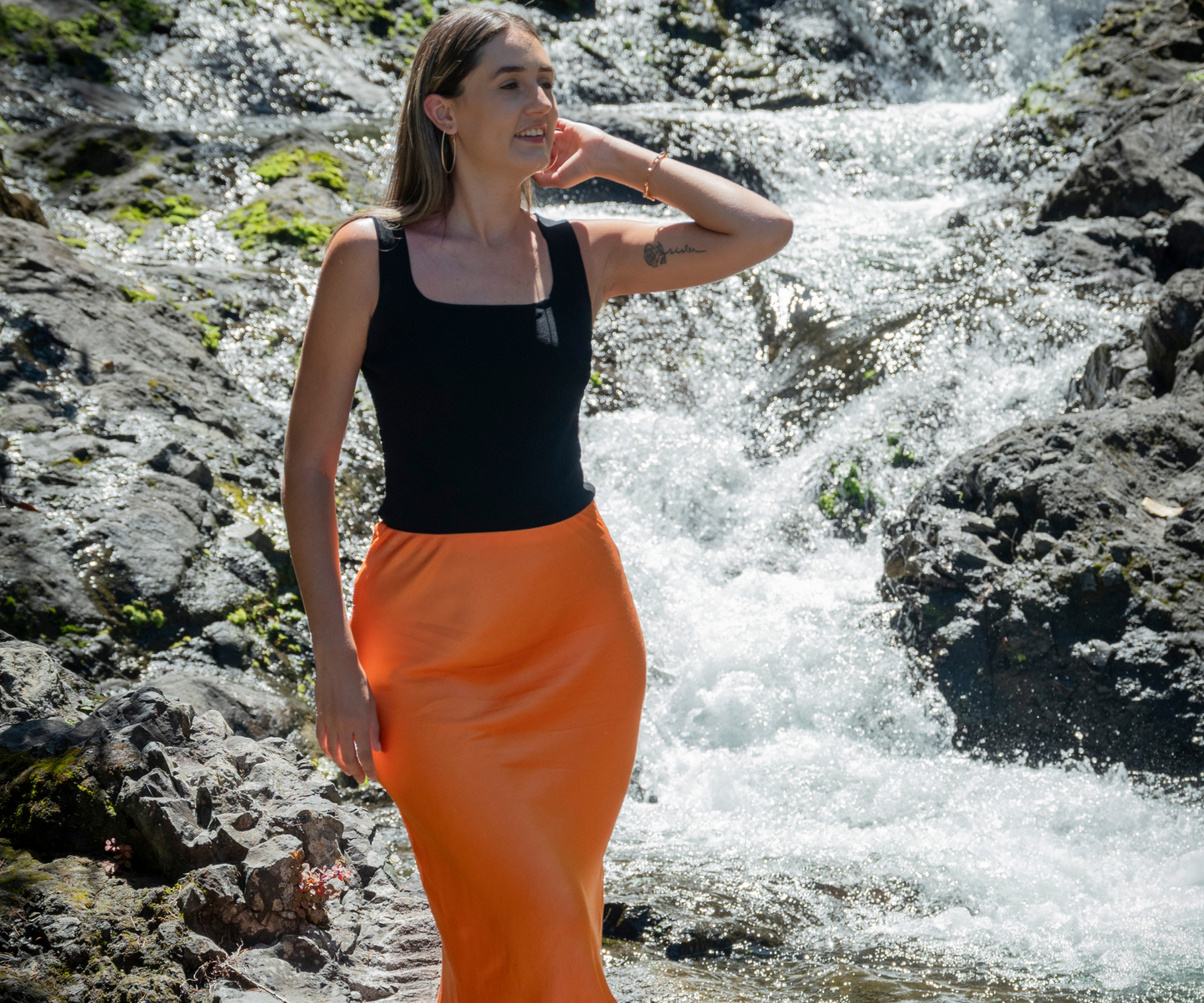 Look jupe effet satiné orange portée avec top noir devant une rivière